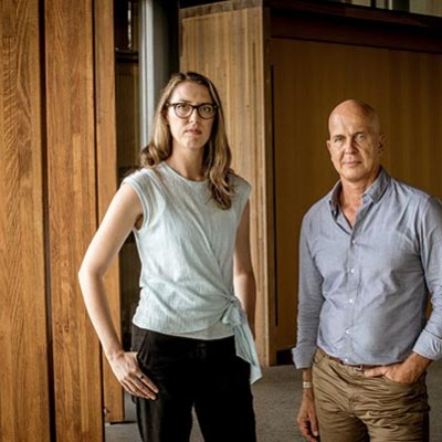Rebecca Ananian-Welsh and Peter Greste standing next to each other in a large lobby with wooden panelling 